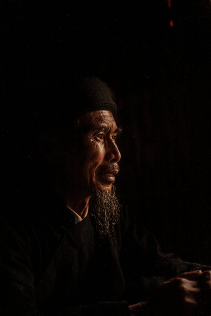 Side view of a senior man with expressive features and a contemplative look in a dark setting.