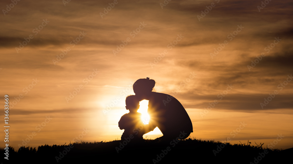 Silhouette of a young mother lovingly kissing her little child o